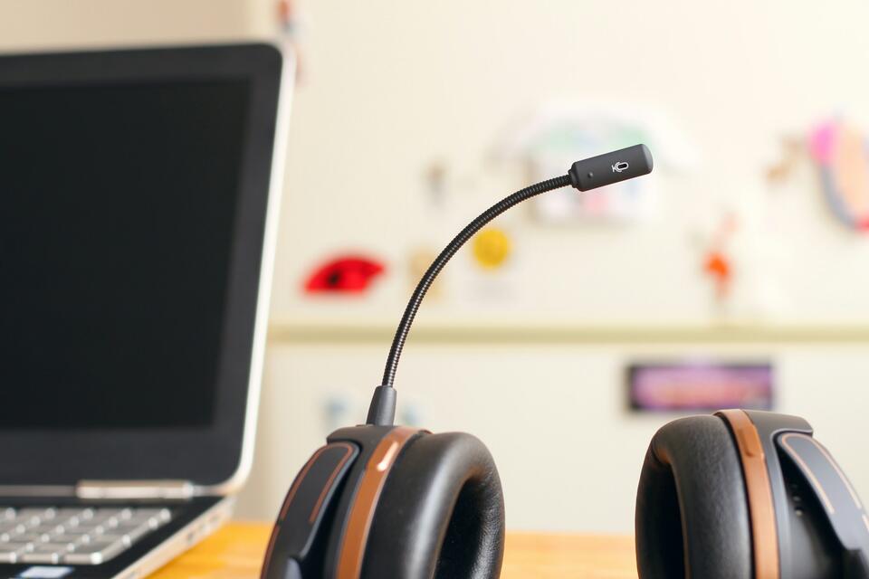 Headset with a boom microphone on a desk beside a laptop