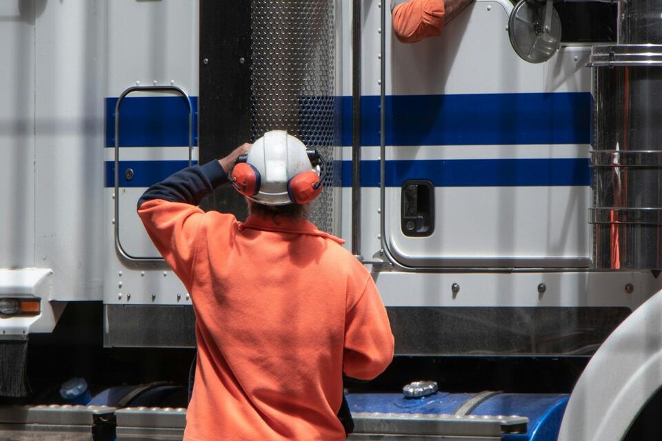 Driver in a hard hat and hearing protection checking a semi truck