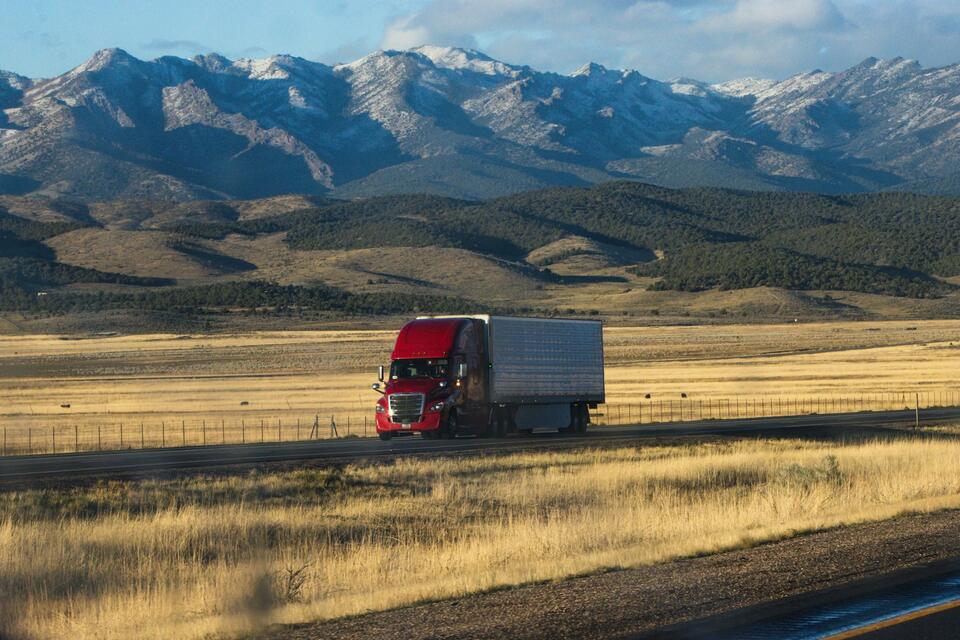 Semi truck crossing golden prairie below snow-capped mountains