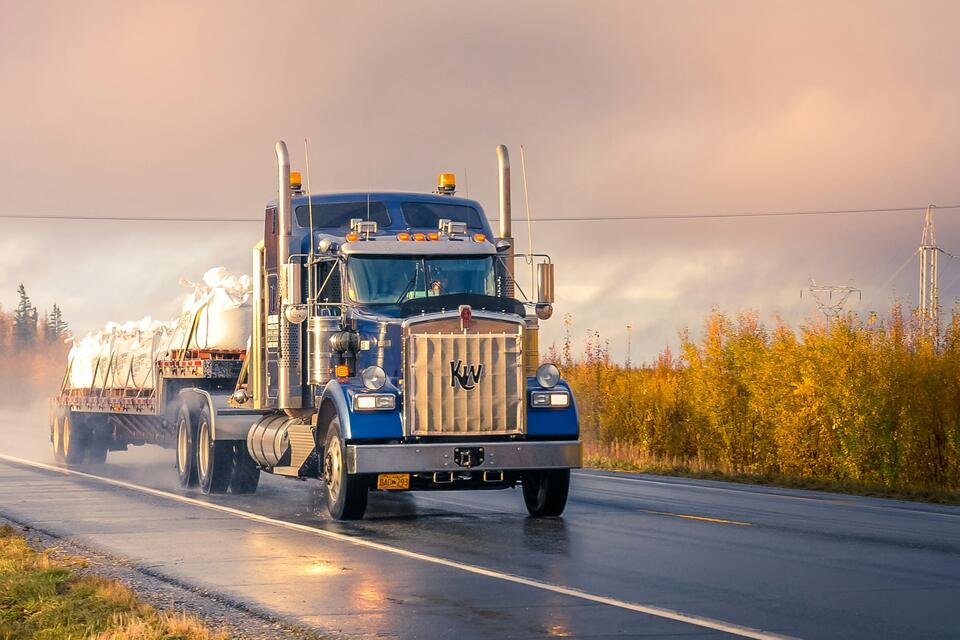 Blue semi truck on a wet two-lane highway at sunrise
