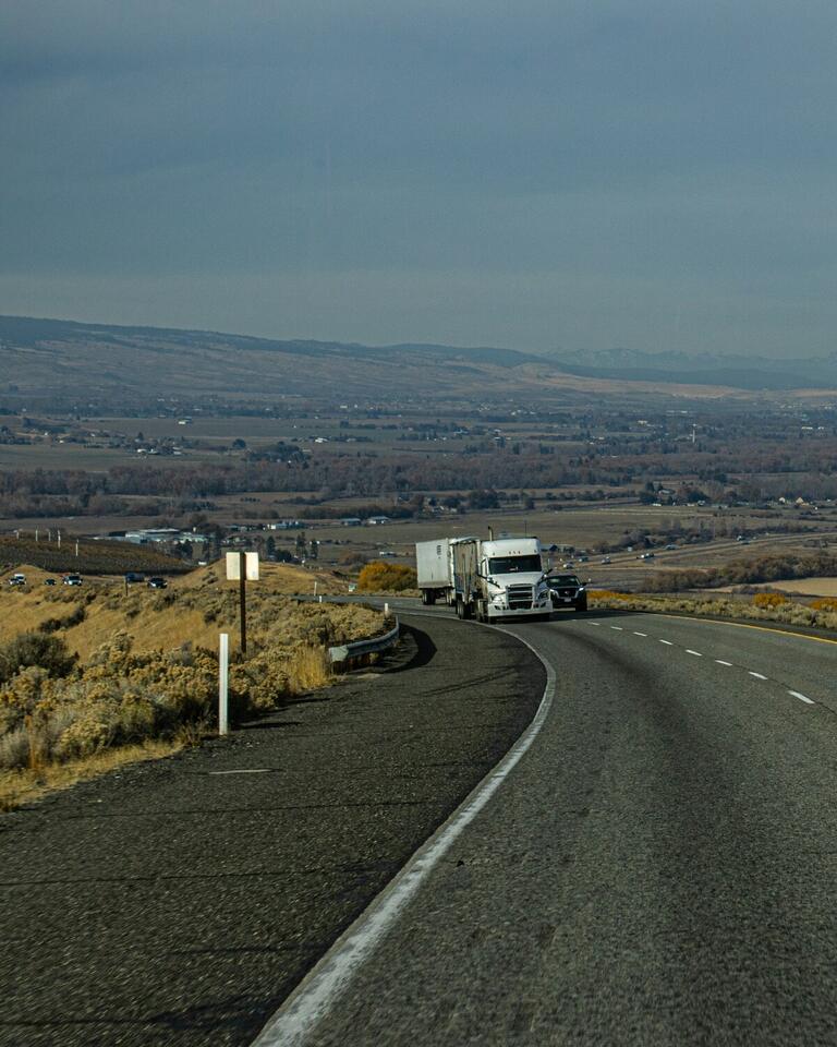 Semi truck rounding a curve on a highway above a wide valley